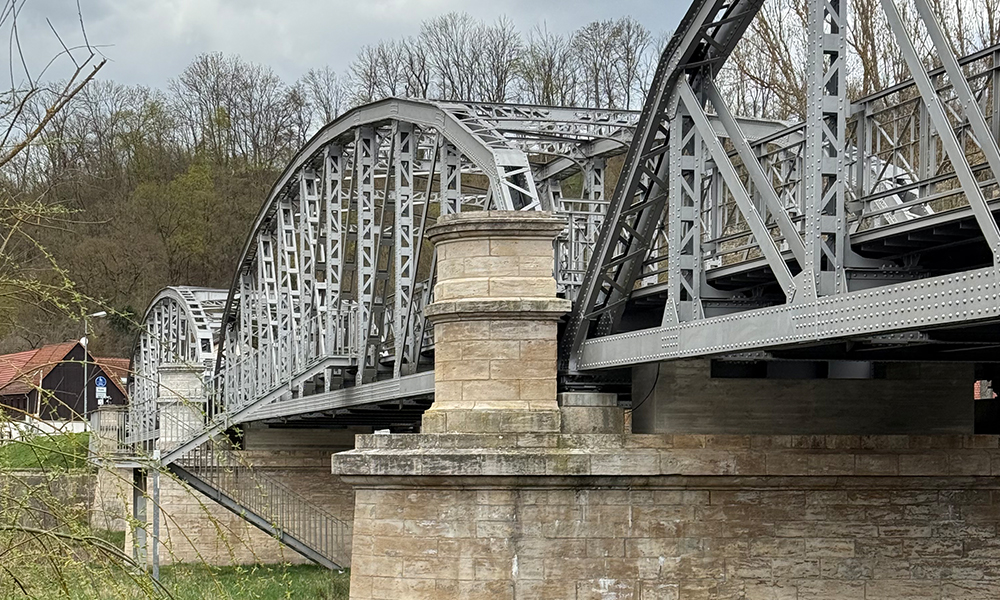 Die historische Brücke als Außenansicht mit Steinsockeln und Stahlträgergerüst
